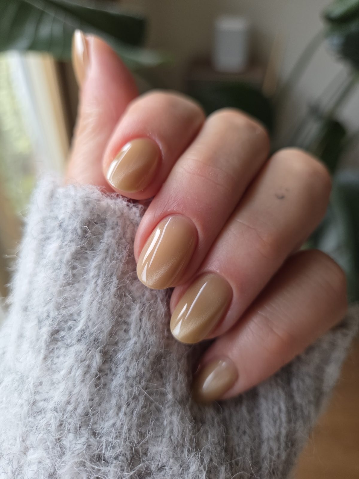 Glanzende karamelkleurige nagels bij een grijze wollen trui
